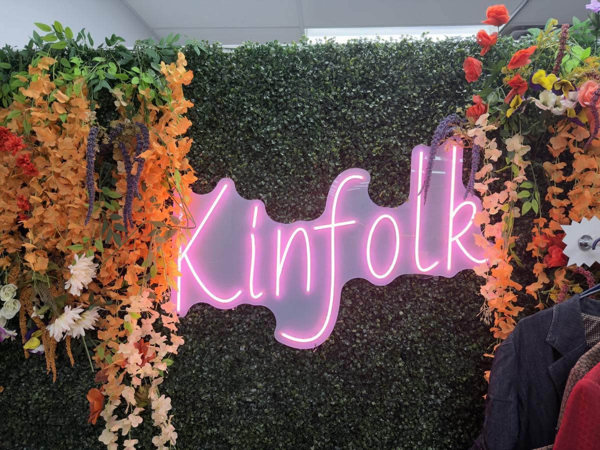 Pink neon 'Kinfolk' sign on a floral greenery wall inside the store