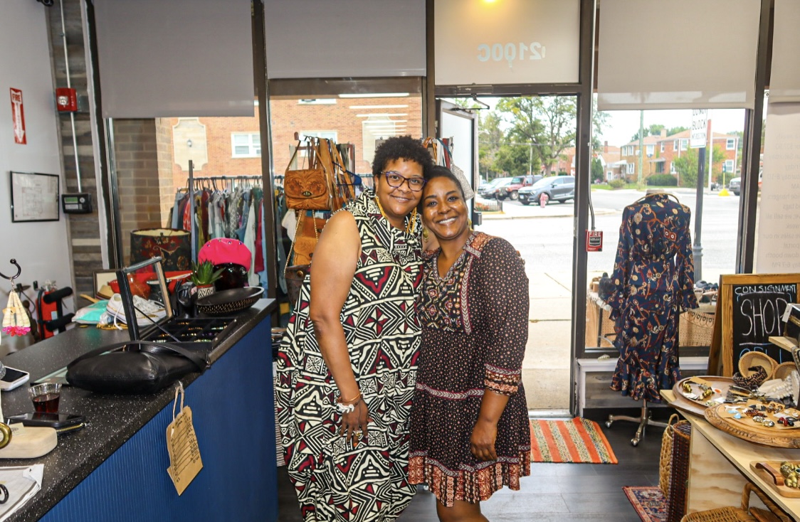 Two Kinfolk Marketplace team members smiling together at the storefront entrance on Roosevelt Road