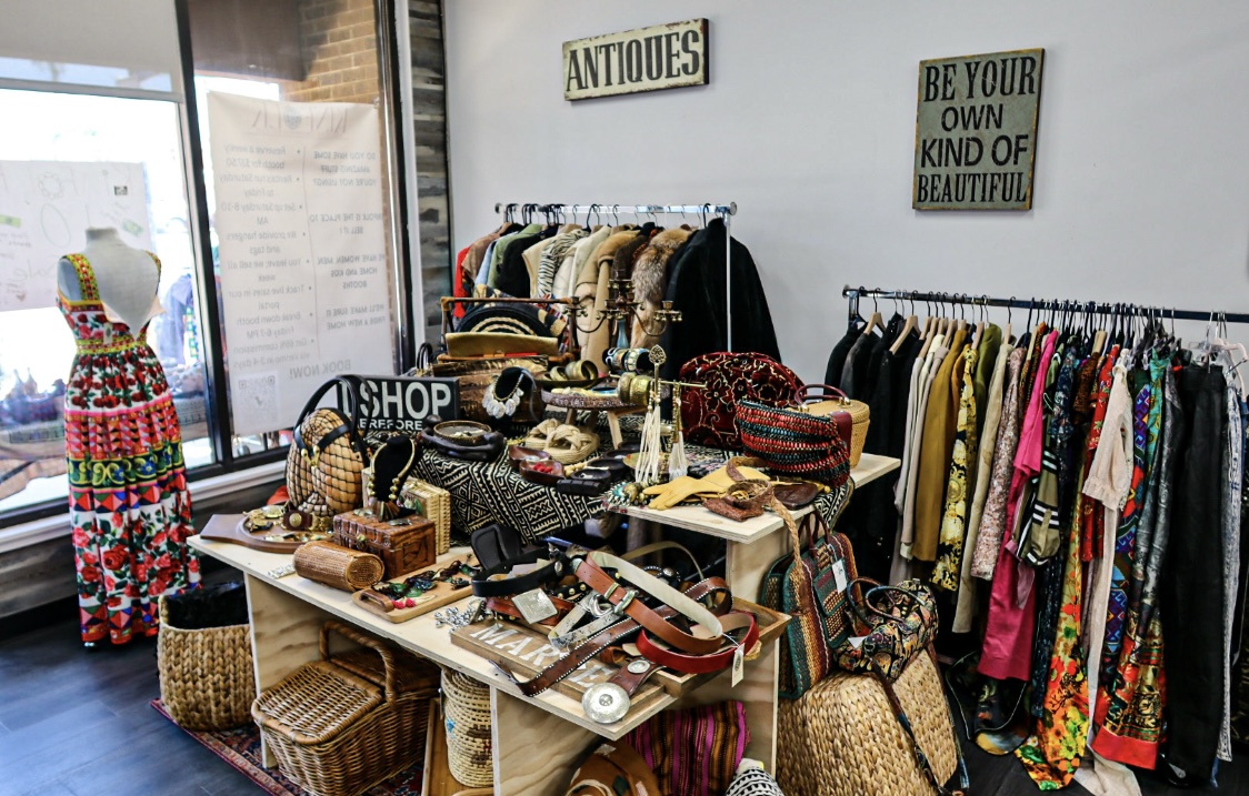 Vendor booth showcasing a vibrant patterned dress on a mannequin alongside antique accessories and a 'Be Your Own Kind of Beautiful' sign