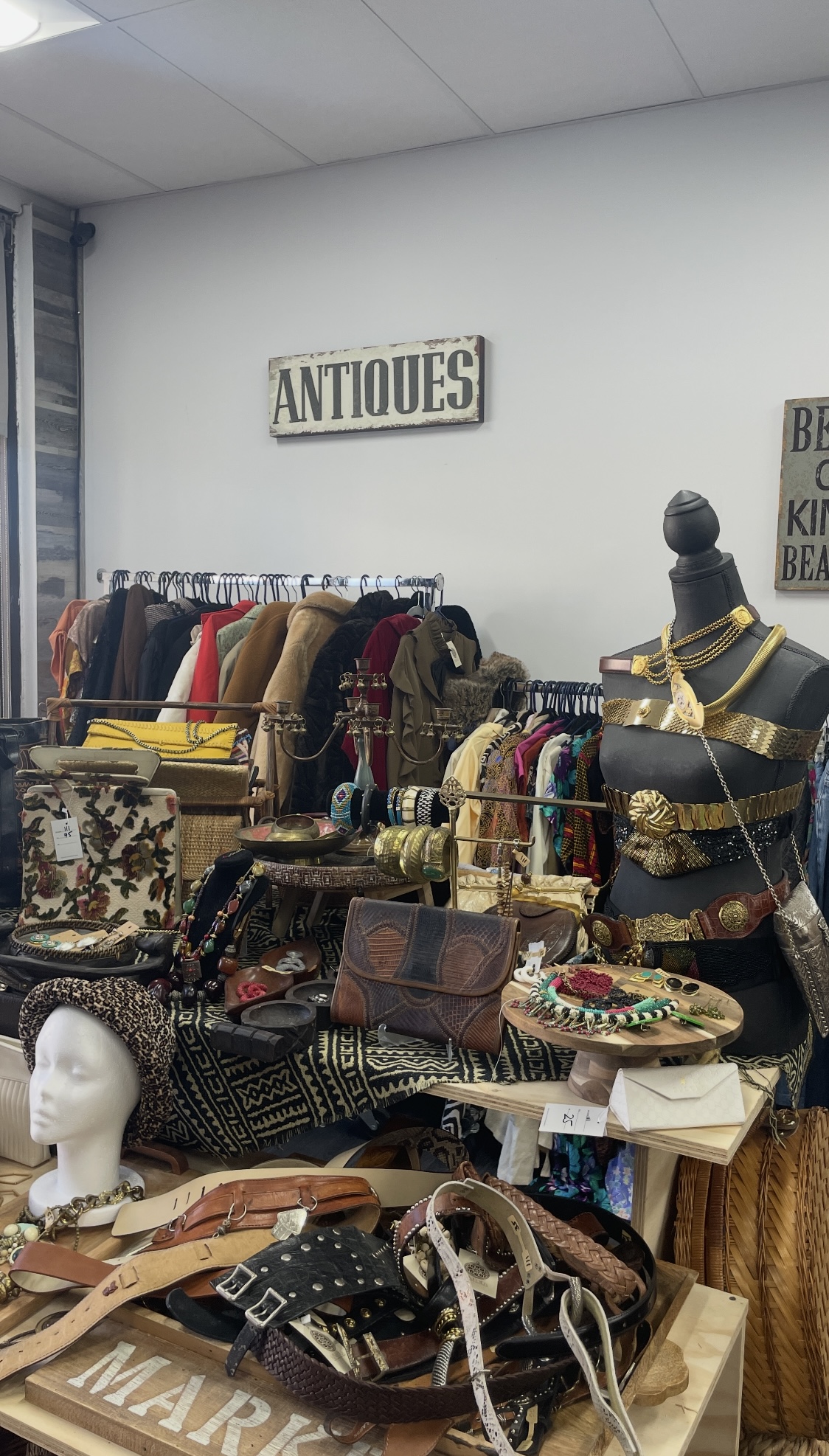 Mannequin styled with layered gold chains, statement belts, and vintage handbags beneath an Antiques sign at Kinfolk Marketplace